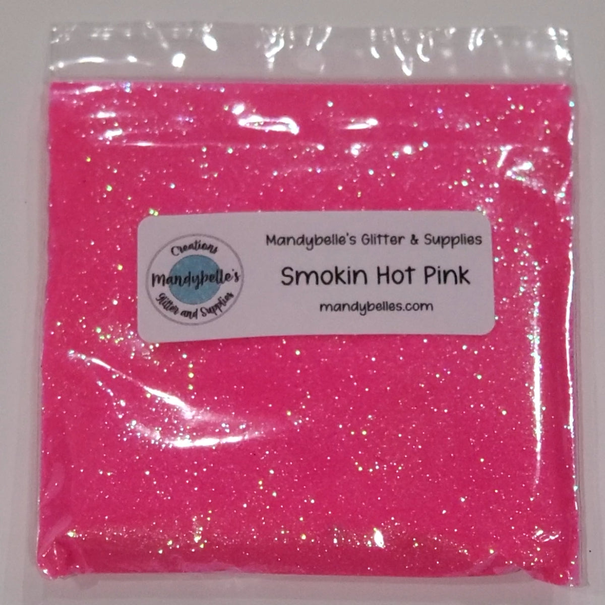 A clear plastic bag filled with bright pink glitter powder, sealed with a white label that reads 'Mandybelle's Glitter & Supplies' and 'Smokin Hot Pink'.