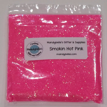 A clear plastic bag filled with bright pink glitter powder, sealed with a white label that reads 'Mandybelle's Glitter & Supplies' and 'Smokin Hot Pink'.