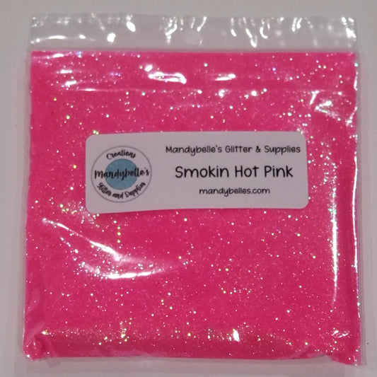 A clear plastic bag filled with bright pink glitter powder, sealed with a white label that reads 'Mandybelle's Glitter & Supplies' and 'Smokin Hot Pink'.